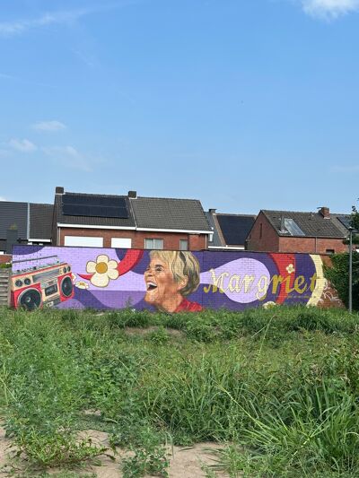 Foto Op de muurschildering lacht Margriet Hermans uitbundig. Foto: Eva van der Klei