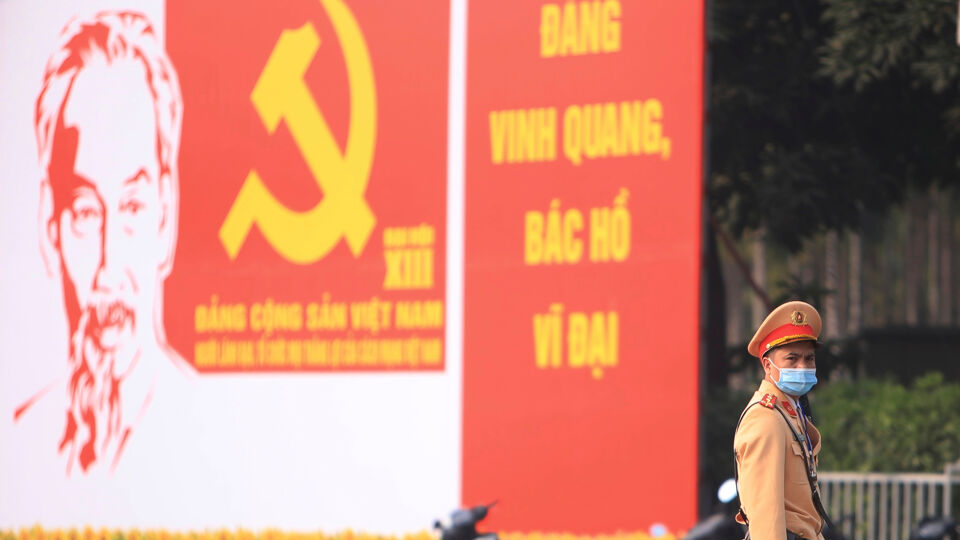 Een politieman op wacht in Hanoi voor grote posters die het partijcongres aankondigen.