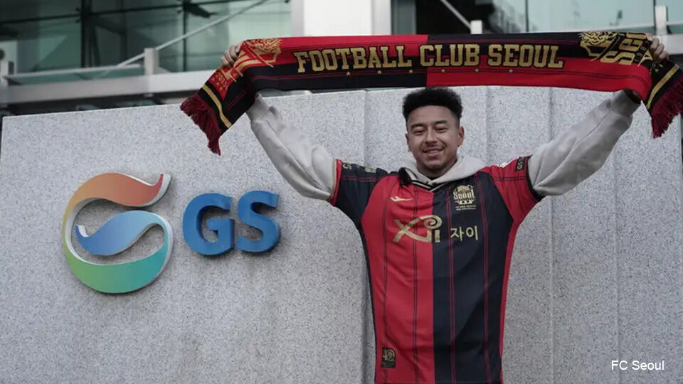 Jesse Lingard poseert met een truitje en een vlag van zijn nieuwe club FC Seoul. De clubkleuren zijn zwart en rood.