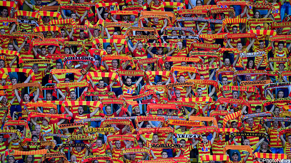 Supporters van Bialystok in geel-rode kleuren met een sjaal in hun handen.